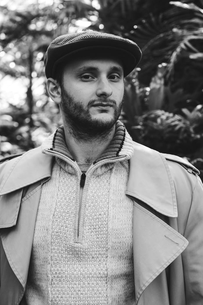 Black and white portrait of a man in vintage fashion with a flat cap and trench coat.