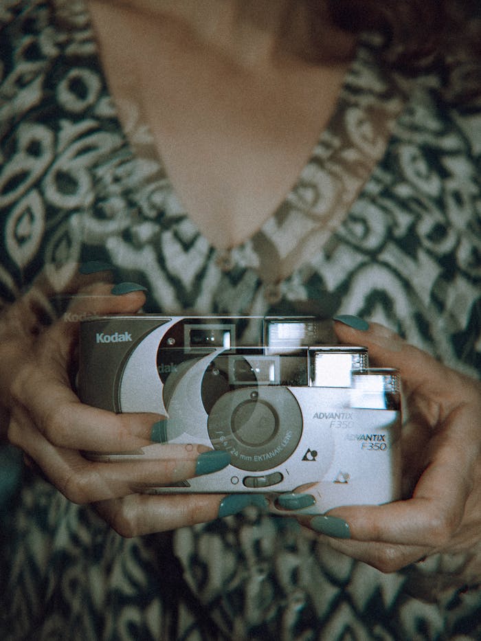 Artistic double exposure photo featuring a vintage Kodak camera held by a person with turquoise nails.