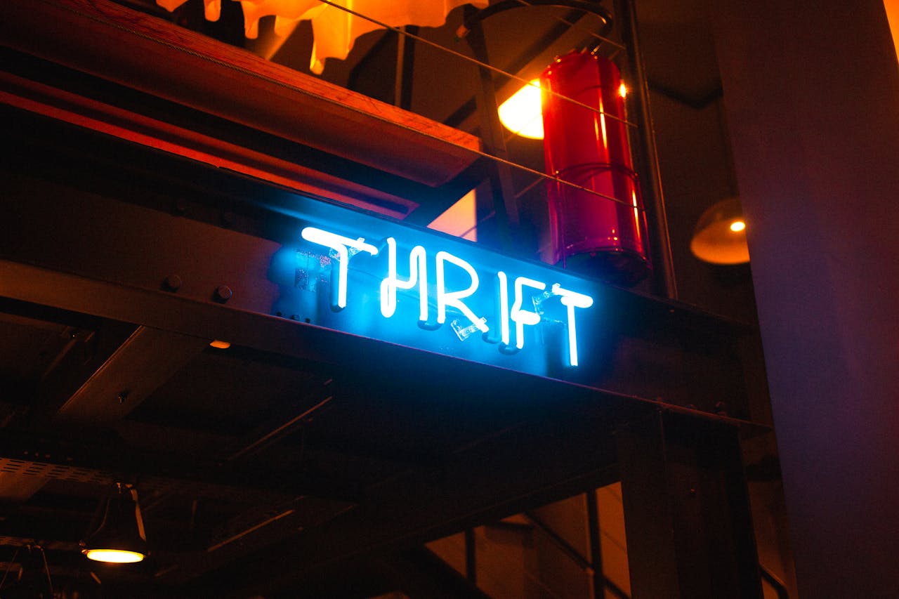 A vibrant neon 'THRIFT' sign glows in an atmospheric indoor setting.